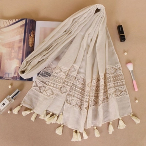 Detailed close-up of beige scarf with geometric lace embroidery and soft fringe tassels