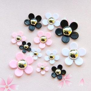 Detailed view of mixed size resin daisy charms in black, white, and pink for DIY jewelry