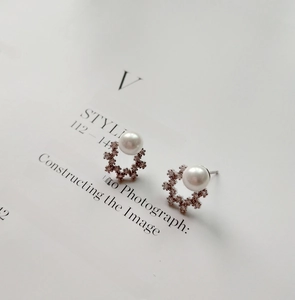 Detail of elegant pearl earring with shimmering snowflake zircon setting on magazine background