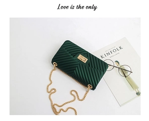 Detailed flat lay of dark green chevron chain bag with golden lock and magazine decor