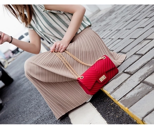 Detail of red matte jelly bag with V-shaped texture and gold chain strap on a model