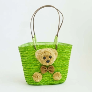 Detalle del bolso de paja verde que muestra el tejido fino y el decorado de osito