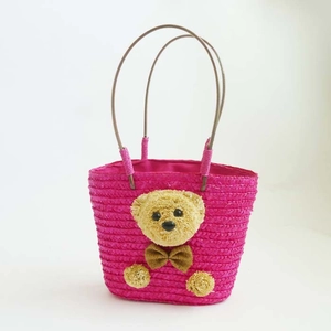 Detalle de bolso de paja rosa fucsia con adorno de osito de peluche y textura tejida