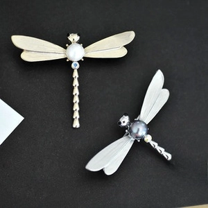 Detailed close-up of a dragonfly brooch featuring a large pearl and matte wings