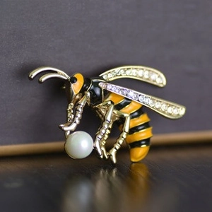 Macro shot of bee brooch with gold finish, crystals, and a round pearl detail