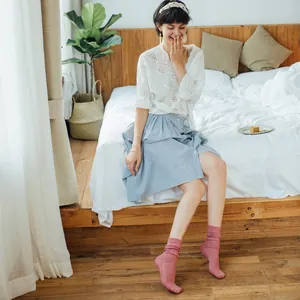 Women's pink knit slouch socks with ribbed texture and ruffle trim in a cozy bedroom setting