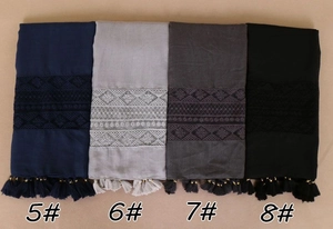 Detail of solid color scarves featuring geometric lace embroidery and beaded tassels
