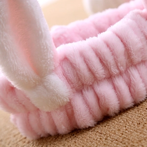 Close-up of pink plush headband with white bunny ears and soft elastic texture