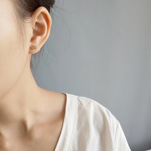 Detail view of gold evil eye stud earring with eyelash texture worn by a model