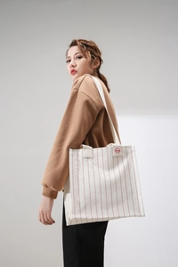 Detail of canvas tote bag featuring red stripes and minimalist circular logo tag