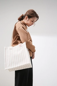 Detail of cream canvas tote bag with red vertical stripes and woven label detail