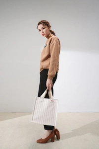 Detail view of white canvas tote bag with red stripes and wide webbing handles on a model