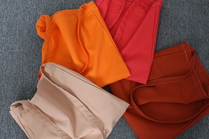 Flat lay of colorful canvas tote bags in orange, pink, brown, and beige with visible stitching