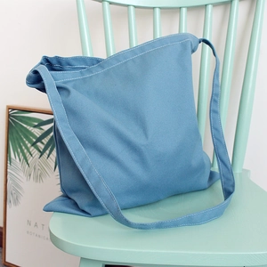 Minimalist fog blue canvas crossbody bag with white stitching detail on a green chair