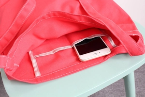 Detail showing inner slip pocket of the pink canvas tote bag holding a white smartphone