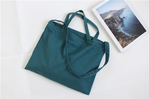 Flat lay of a dark green canvas tote bag with white stitching and a magazine