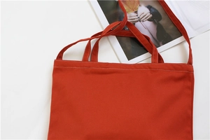 Detail of brick red canvas tote showing reinforced white stitching and dual strap design