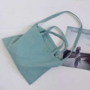 Detail of light blue canvas tote bag with dual handles and shoulder strap on grey background