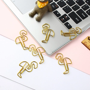 Creative flamingo shaped golden metal paper clips scattered on a desk with a laptop
