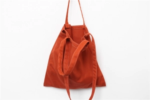 Detail of orange canvas tote bag showing white contrast stitching and dual strap design