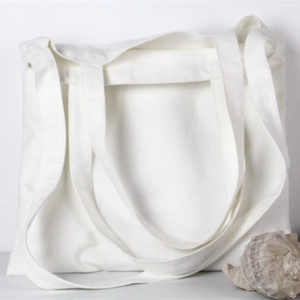 Minimalist white canvas tote bag leaning against a wall with a natural shell prop