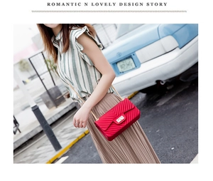 Detail of red V-quilted crossbody bag with gold chain strap and twist lock on model