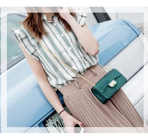 Detail of dark green V-quilted chain bag with gold rotary lock and glossy finish
