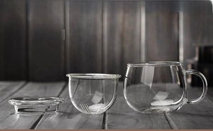 Three-piece heat-resistant glass tea set with cup, infuser filter and lid on wood