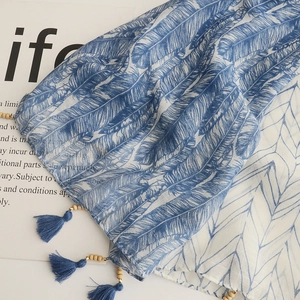 Detail of blue and white scarf featuring feather patterns with wooden beads and tassels