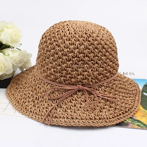 Close-up of a hand-woven brown straw hat featuring a delicate bow tie on a white surface