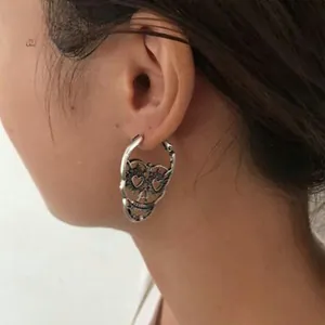Detailed view of vintage silver skull earrings with heart-shaped eyes on model ear