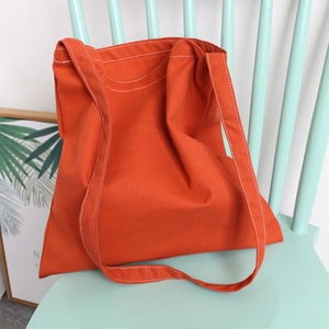 Close-up of bright orange canvas tote bag showing white contrast stitching and thick texture