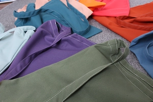 Close-up of colorful canvas tote bags showing reinforced white stitching and fabric texture