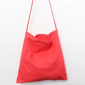 Detail of red canvas tote bag showing white stitching craftsmanship and slim shoulder straps