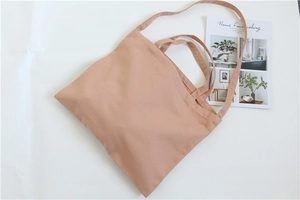 Detail of light brown canvas tote bag with dual shoulder straps on a clean background