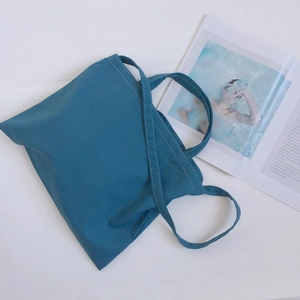 Detail of teal cotton canvas tote bag with white stitching and shoulder straps on white background