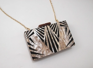 Detail of geometric acrylic clutch bag with sunburst pattern and gold metal chain strap