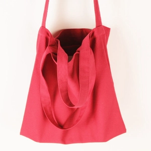Detail of red canvas tote bag featuring dual shoulder straps and sturdy hand-held handle