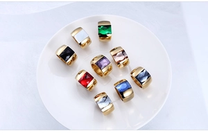 Close-up of golden titanium steel rings with multi-color gemstones on white plate