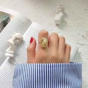 Close-up of a gold oval Virgin Mary medallion ring on hand with vintage props