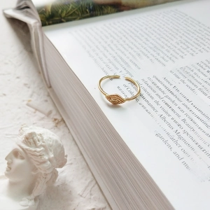 Detail of gold evil eye open ring resting on a vintage book with artistic plaster decor