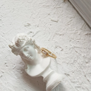 Detailed shot of golden rectangular purple gemstone ring displayed on a white plaster statue