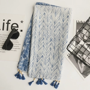 Flat lay of blue and white leaf print linen scarf with tassels and fashion accessories