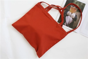 Close-up of orange-red canvas tote bag with precise double-row stitching and shoulder strap