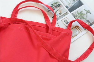 Close-up of red canvas tote bag showing reinforced wide straps and white stitching details