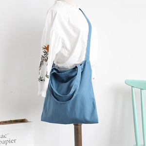 Blue canvas tote bag with long straps for shoulder and crossbody wear on a model