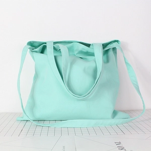 Detail of mint green canvas tote bag with dual handles and long shoulder strap