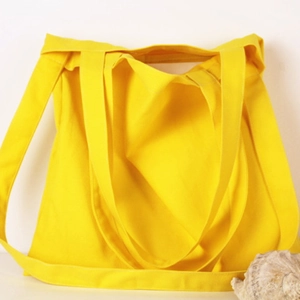 Detailed view of yellow canvas tote bag texture with wide shoulder straps and shell decor