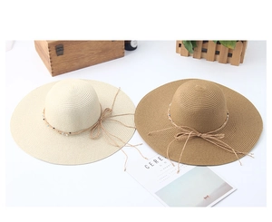Detail of wide brim straw hats with delicate bow tie and colorful beads on white table