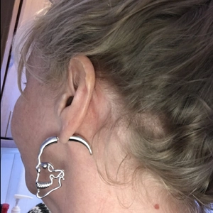 Close-up of a large silver hollow skull stud earring on an ear for scale and detail